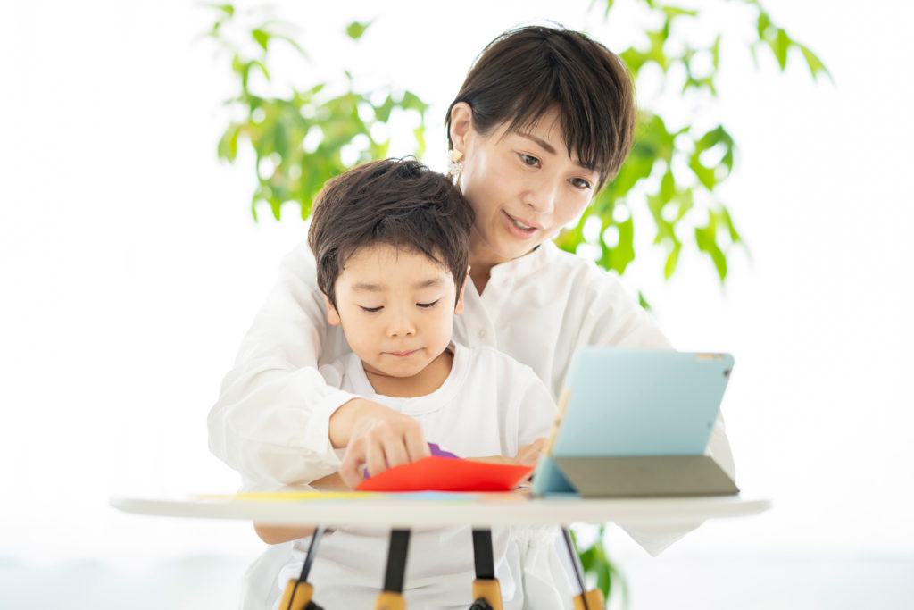 タブレットPCを見ながら折り紙をする親子の写真 タブレットPCを見ながら折り紙をする親子